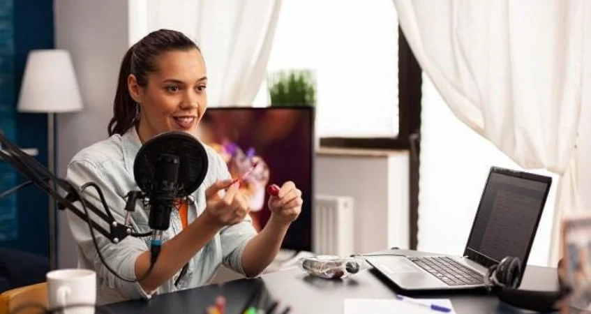 A woman podcasting or holding a virtual conference from a table with a laptop and microphone